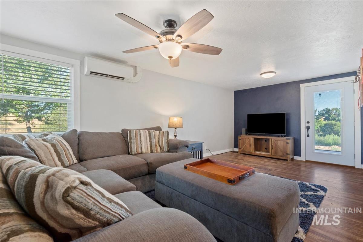Living area with wood finished floors, a wall mounted AC, and a ceiling fan
