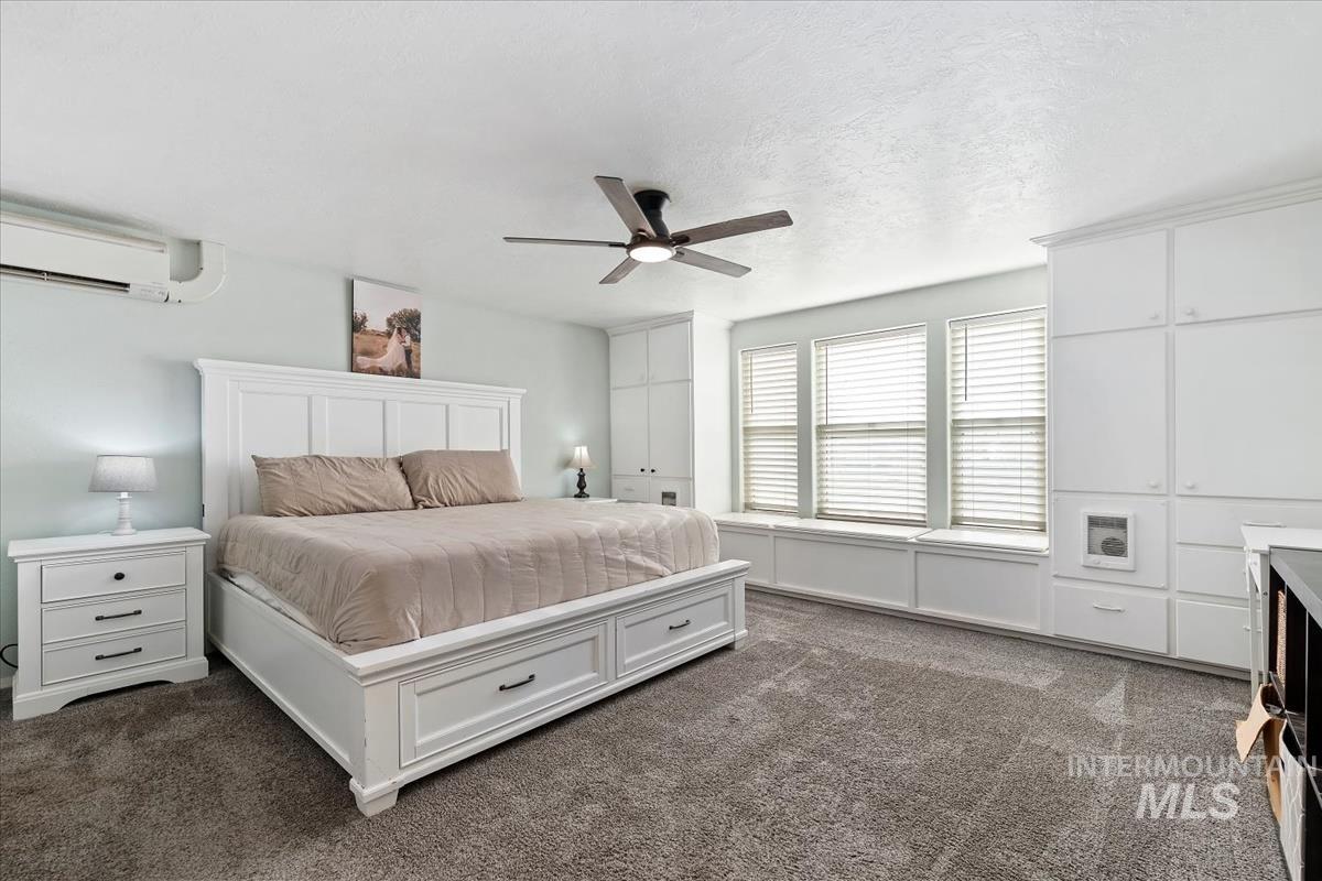 Bedroom with dark carpet, a textured ceiling, an AC wall unit, and ceiling fan