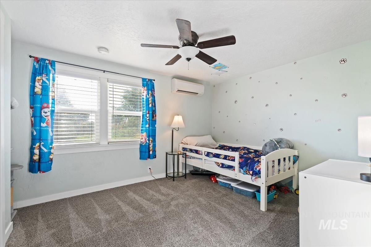 Carpeted bedroom featuring a textured ceiling, a ceiling fan, and a wall unit AC