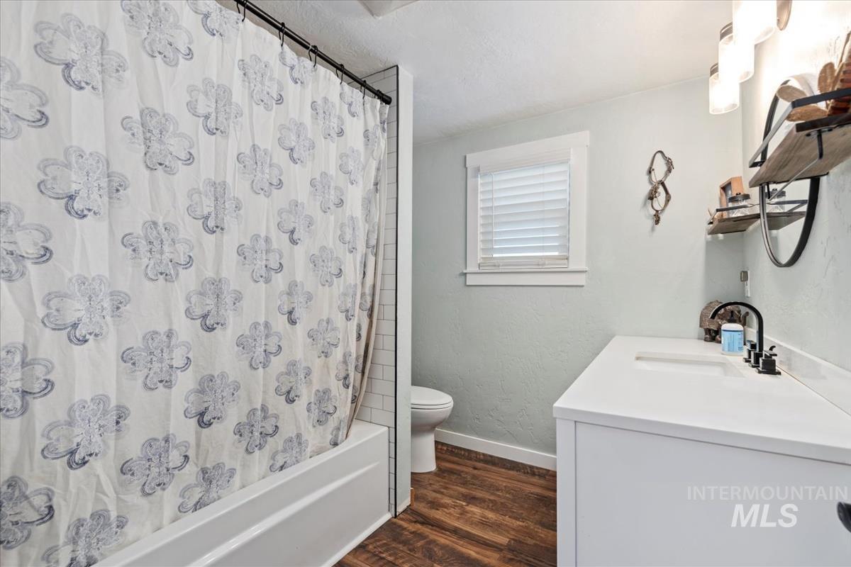 Bathroom featuring wood finished floors, a textured wall, vanity, shower / bathtub combination with curtain, and a textured ceiling