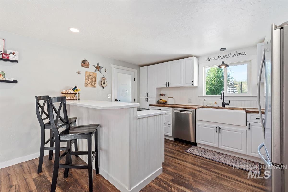 Kitchen featuring stainless steel appliances, a peninsula, white cabinetry, dark wood-type flooring, and a kitchen breakfast bar