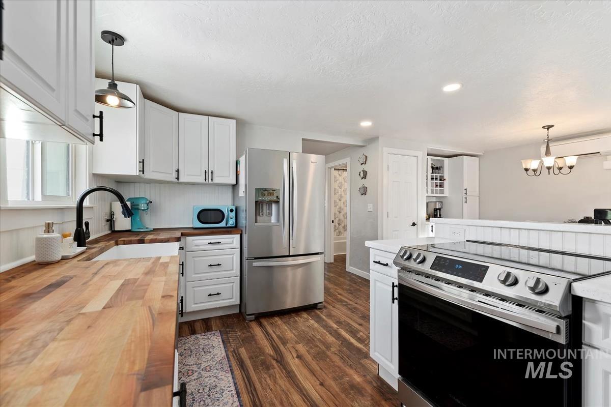 Kitchen with butcher block countertops, stainless steel appliances, dark wood-style floors, white cabinets, and hanging light fixtures