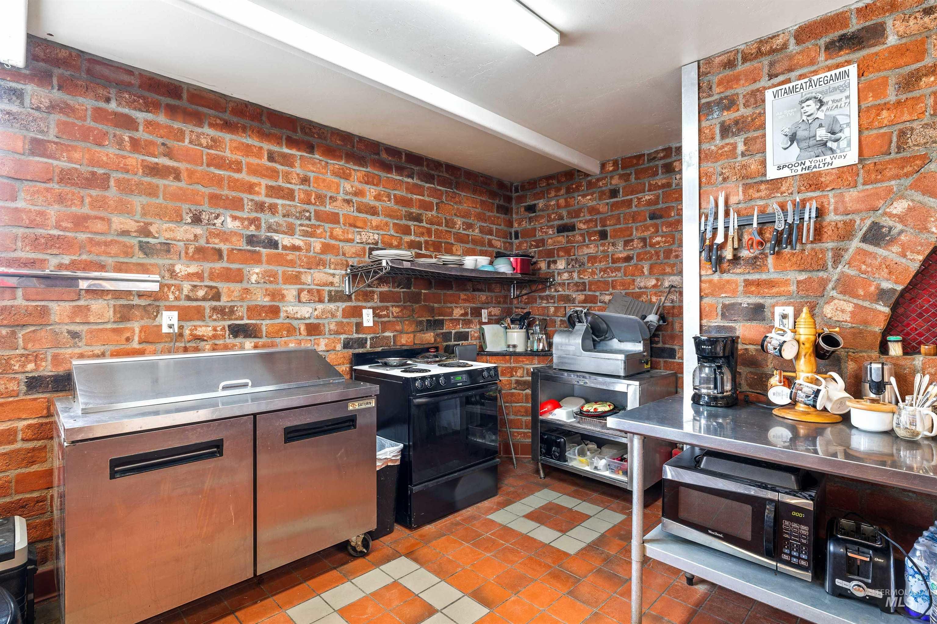 Kitchen with stainless steel countertops, brick wall, dark tile patterned flooring, slide in range oven, and stainless steel microwave