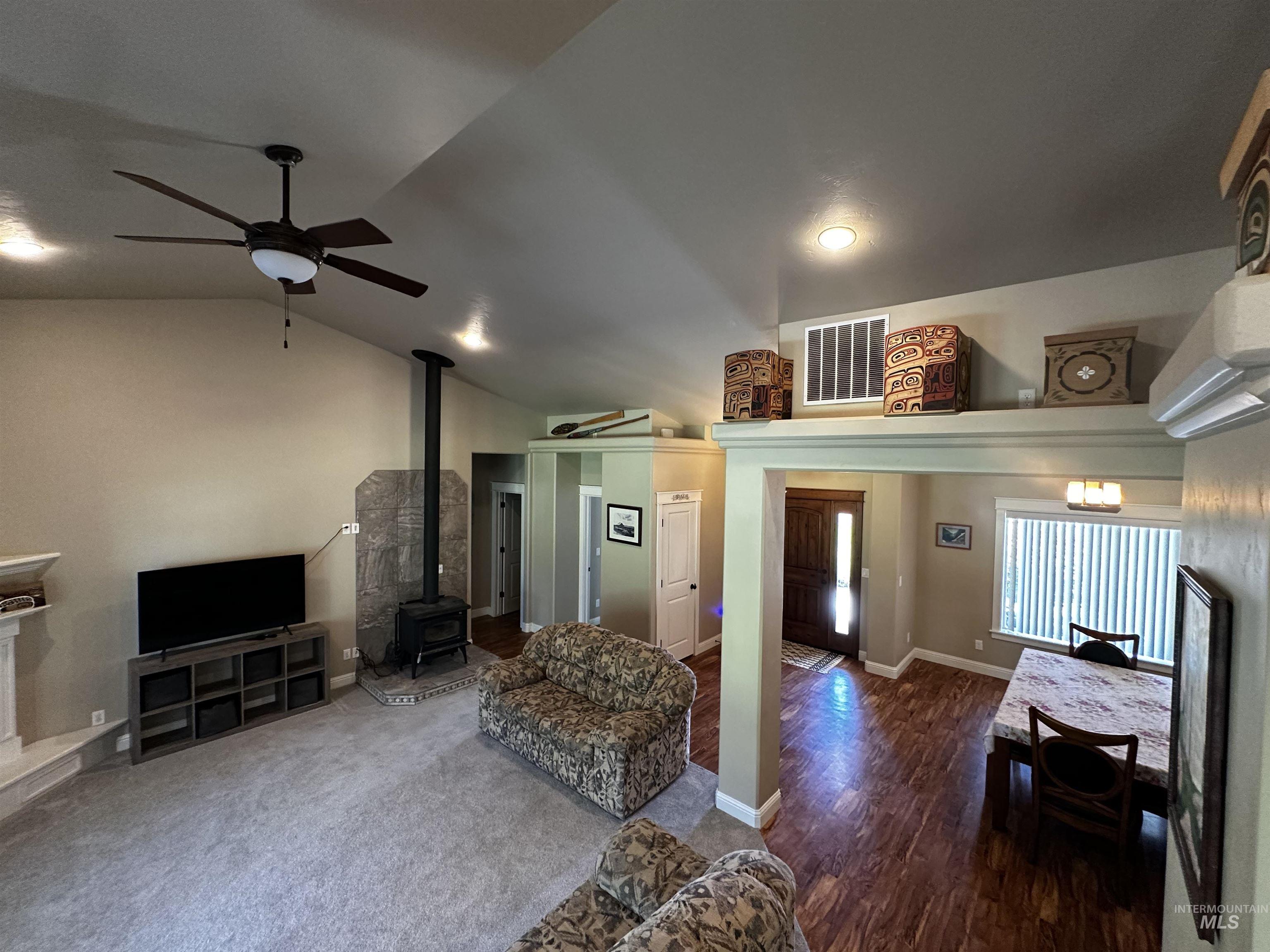 Living area with a wood stove, vaulted ceiling, ceiling fan, and dark wood-style floors