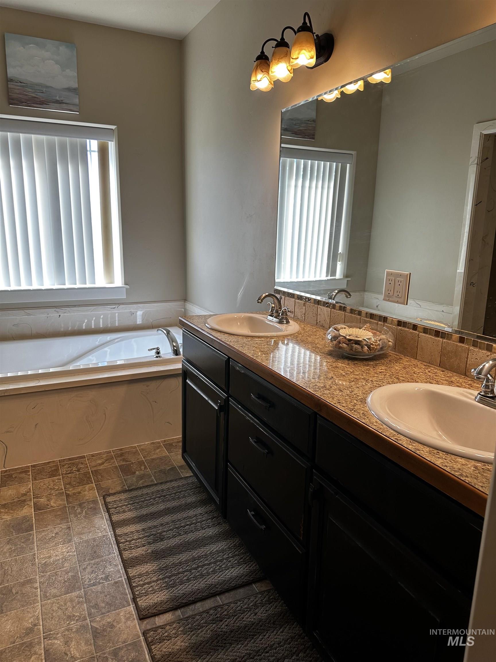 Full bath with healthy amount of natural light, a garden tub, and dark stone finish floors