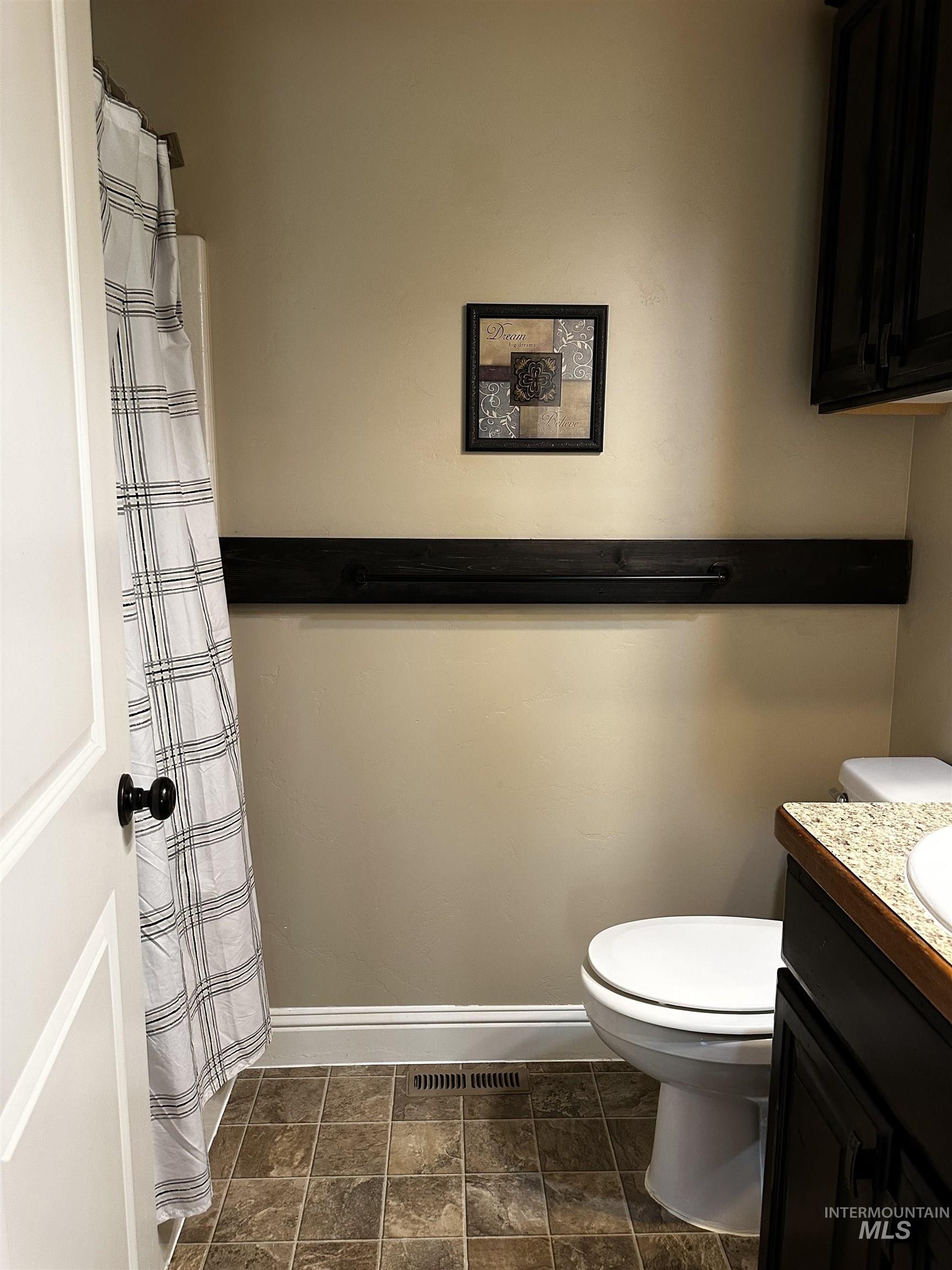 Bathroom featuring vanity, a shower with shower curtain, and dark stone finish flooring