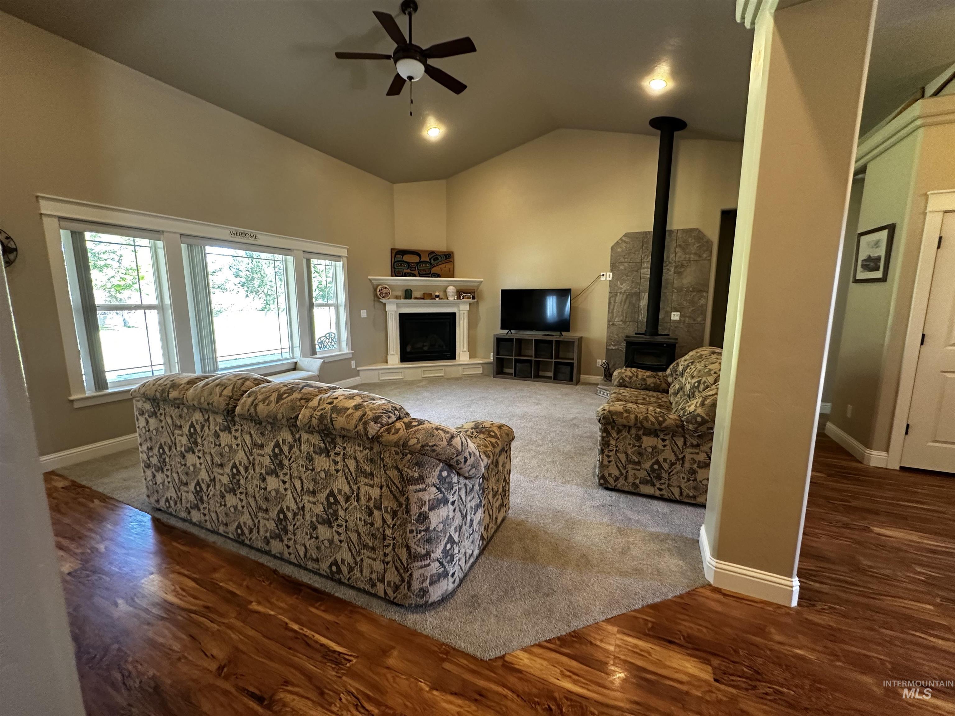 Living area featuring dark wood-type flooring, a fireplace, a wood stove, a ceiling fan, and high vaulted ceiling