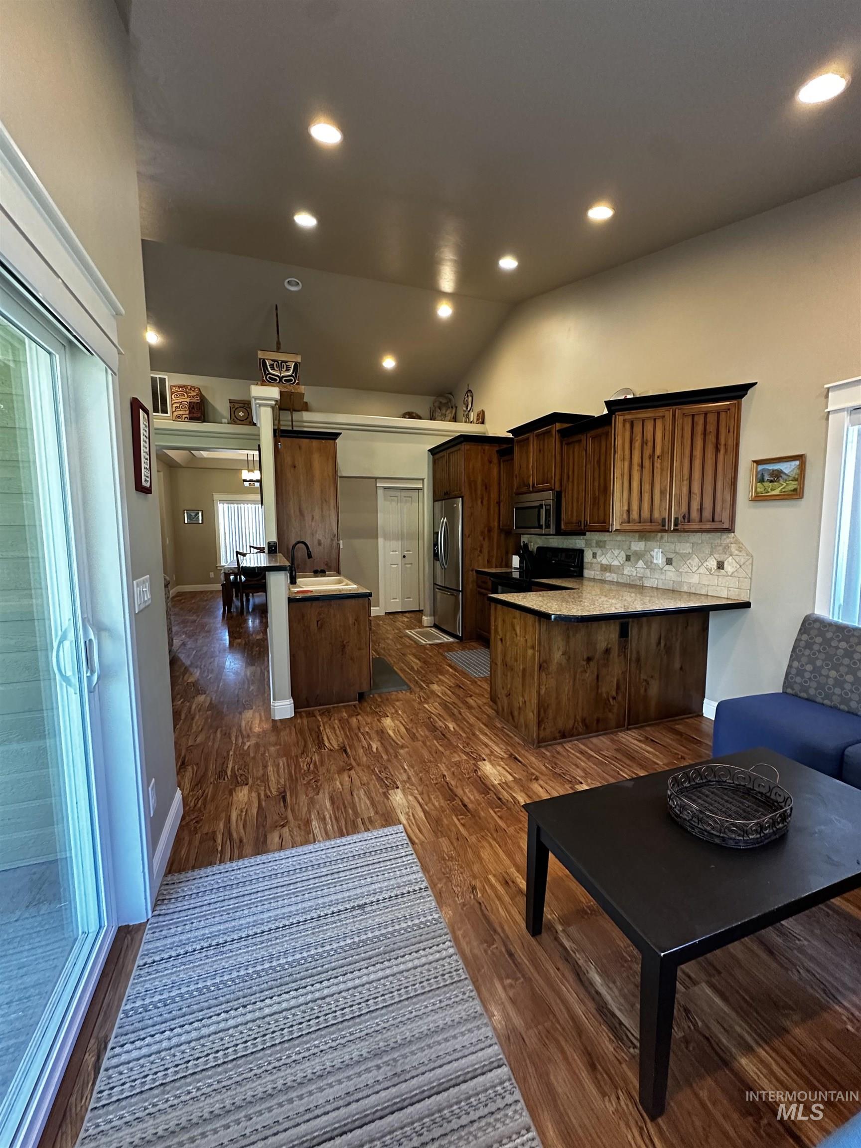 Kitchen with lofted ceiling, a peninsula, decorative backsplash, dark wood-type flooring, and recessed lighting