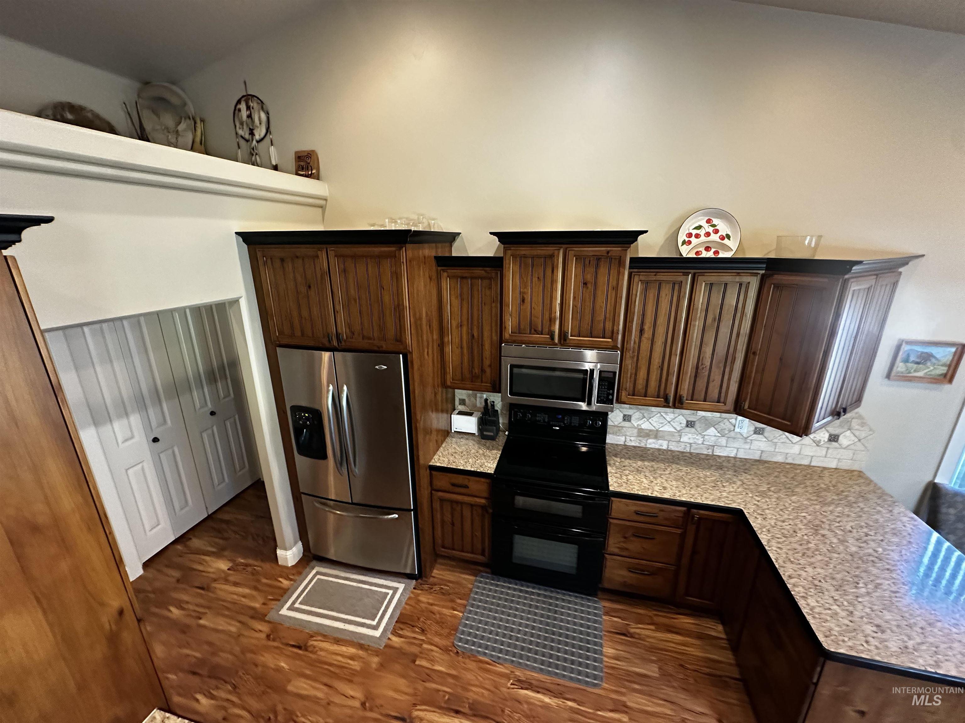 Kitchen with appliances with stainless steel finishes, dark brown cabinetry, dark wood-type flooring, and tasteful backsplash