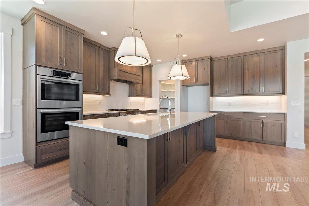 Kitchen featuring pendant lighting, tasteful backsplash, stainless steel double oven, a kitchen island with sink, and recessed lighting