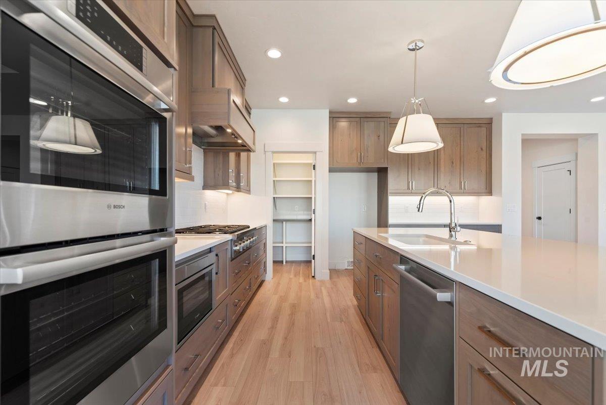Kitchen featuring stainless steel appliances, pendant lighting, light wood-type flooring, brown cabinetry, and recessed lighting