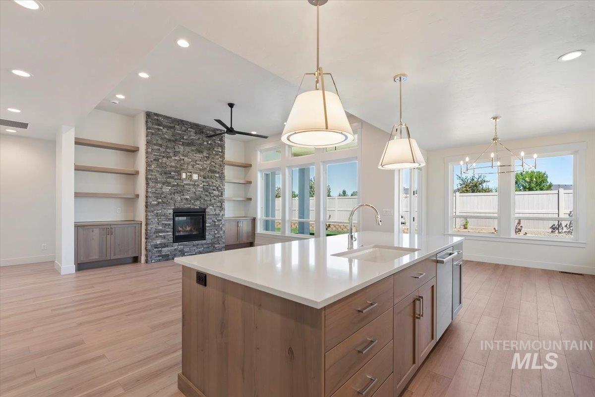 Kitchen with brown cabinets, light wood-type flooring, a fireplace, hanging light fixtures, and recessed lighting