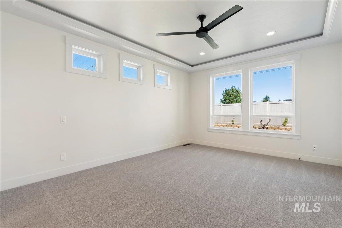 Spare room with a raised ceiling, healthy amount of natural light, light carpet, a ceiling fan, and recessed lighting