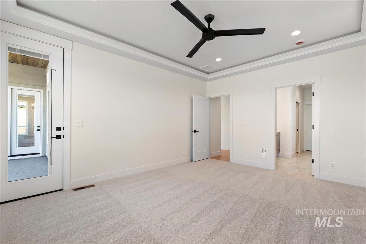 Unfurnished bedroom featuring light colored carpet, recessed lighting, a raised ceiling, connected bathroom, and a ceiling fan