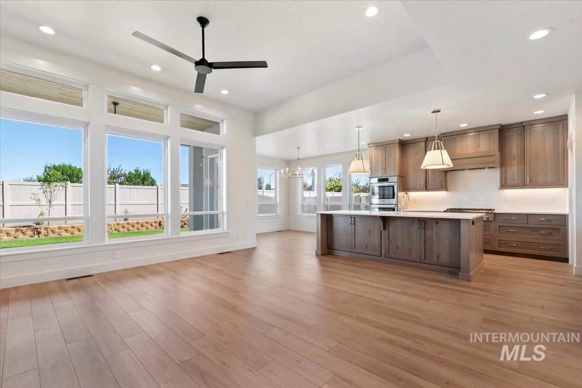 Kitchen featuring hanging light fixtures, light wood-style flooring, ceiling fan, an island with sink, and open floor plan