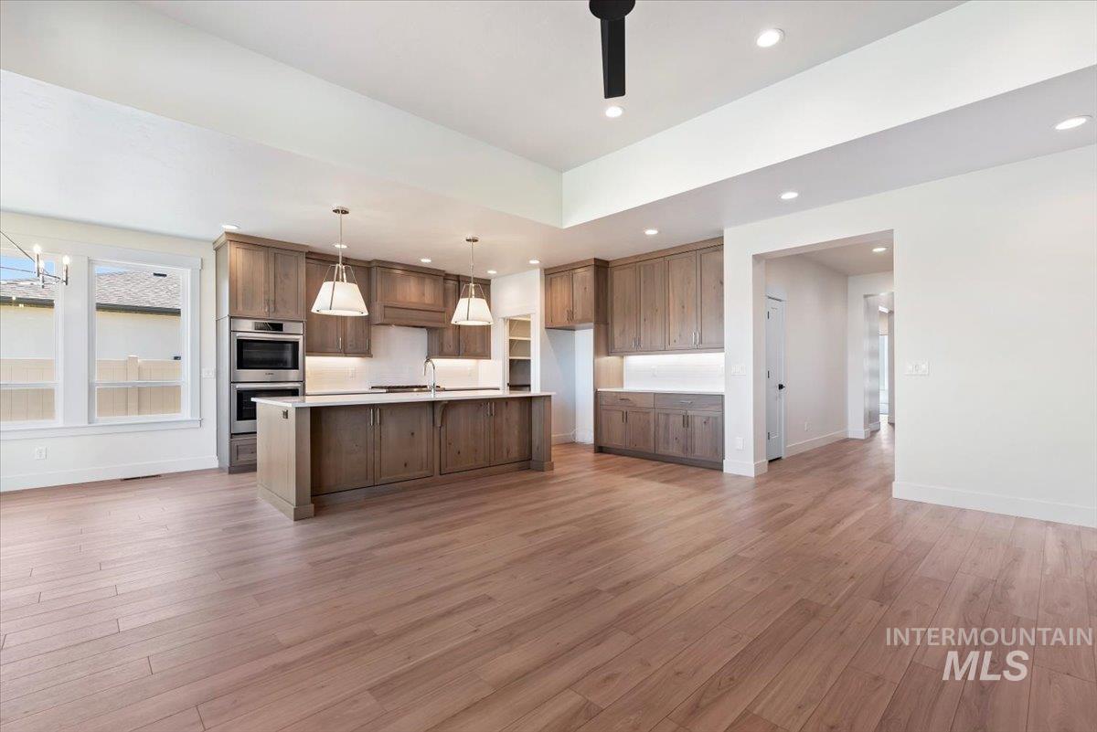 Kitchen with light wood-style floors, decorative light fixtures, recessed lighting, an island with sink, and double oven
