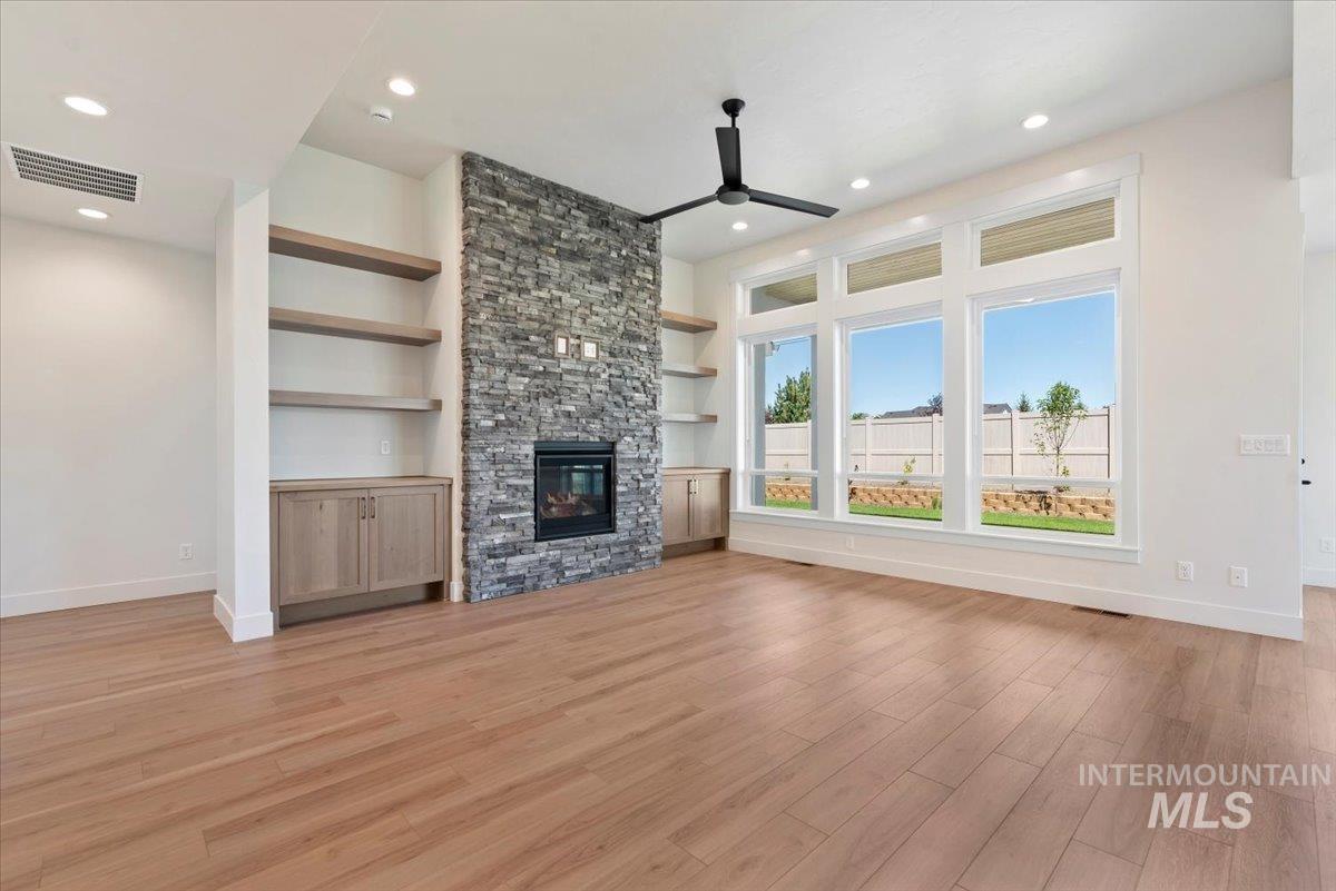 Unfurnished living room featuring a stone fireplace, ceiling fan, built in features, light wood finished floors, and recessed lighting