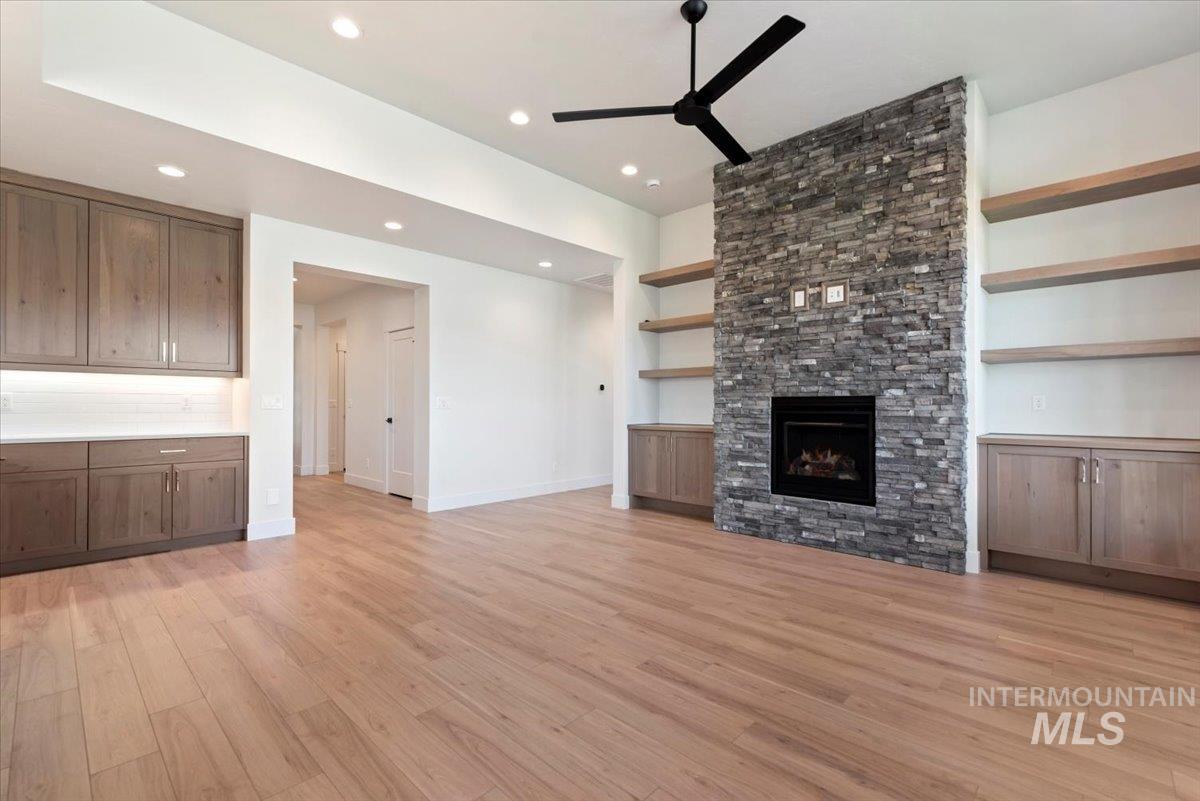 Unfurnished living room with light wood-style floors, a ceiling fan, a stone fireplace, and recessed lighting