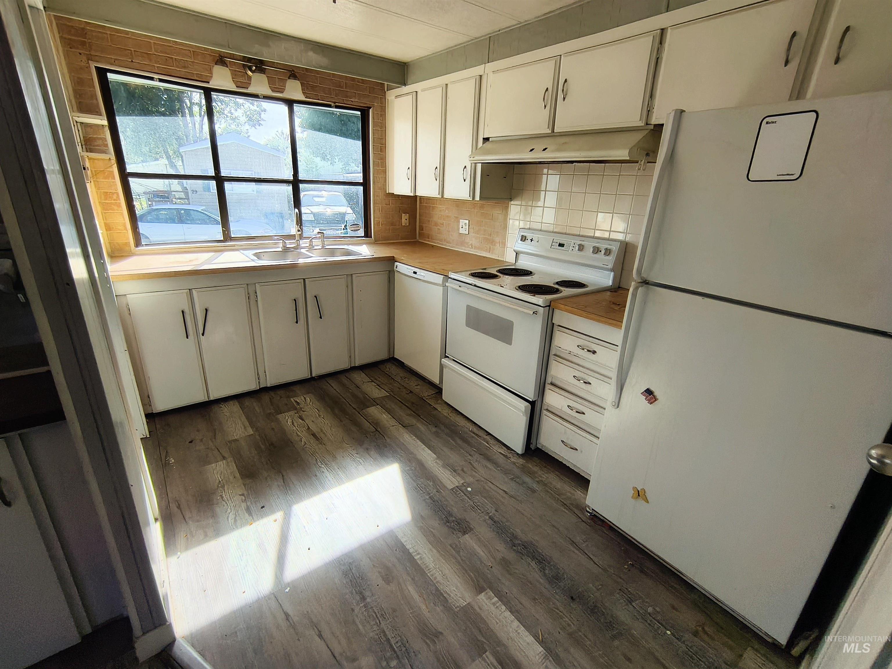 Kitchen featuring white appliances, light countertops, white cabinets, tasteful backsplash, and dark wood-style floors