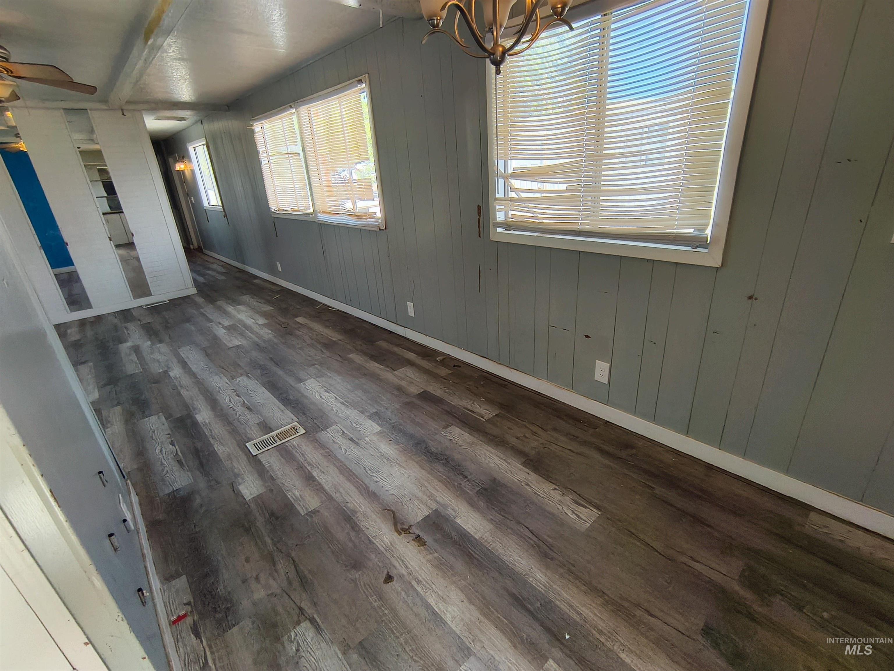 Unfurnished dining area featuring dark wood-type flooring, wood walls, and a chandelier