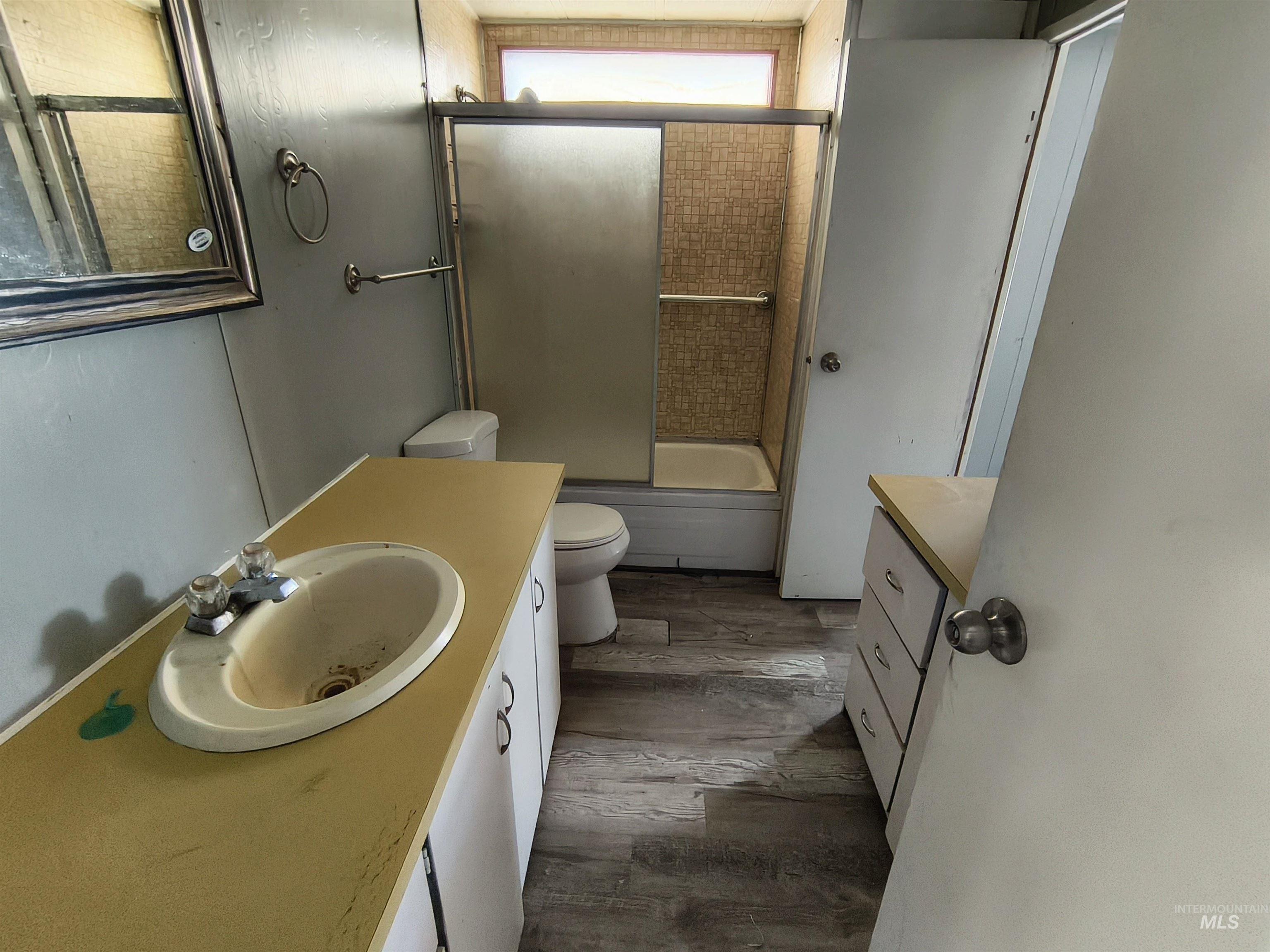 Bathroom with vanity, bath / shower combo with glass door, and dark wood-style flooring