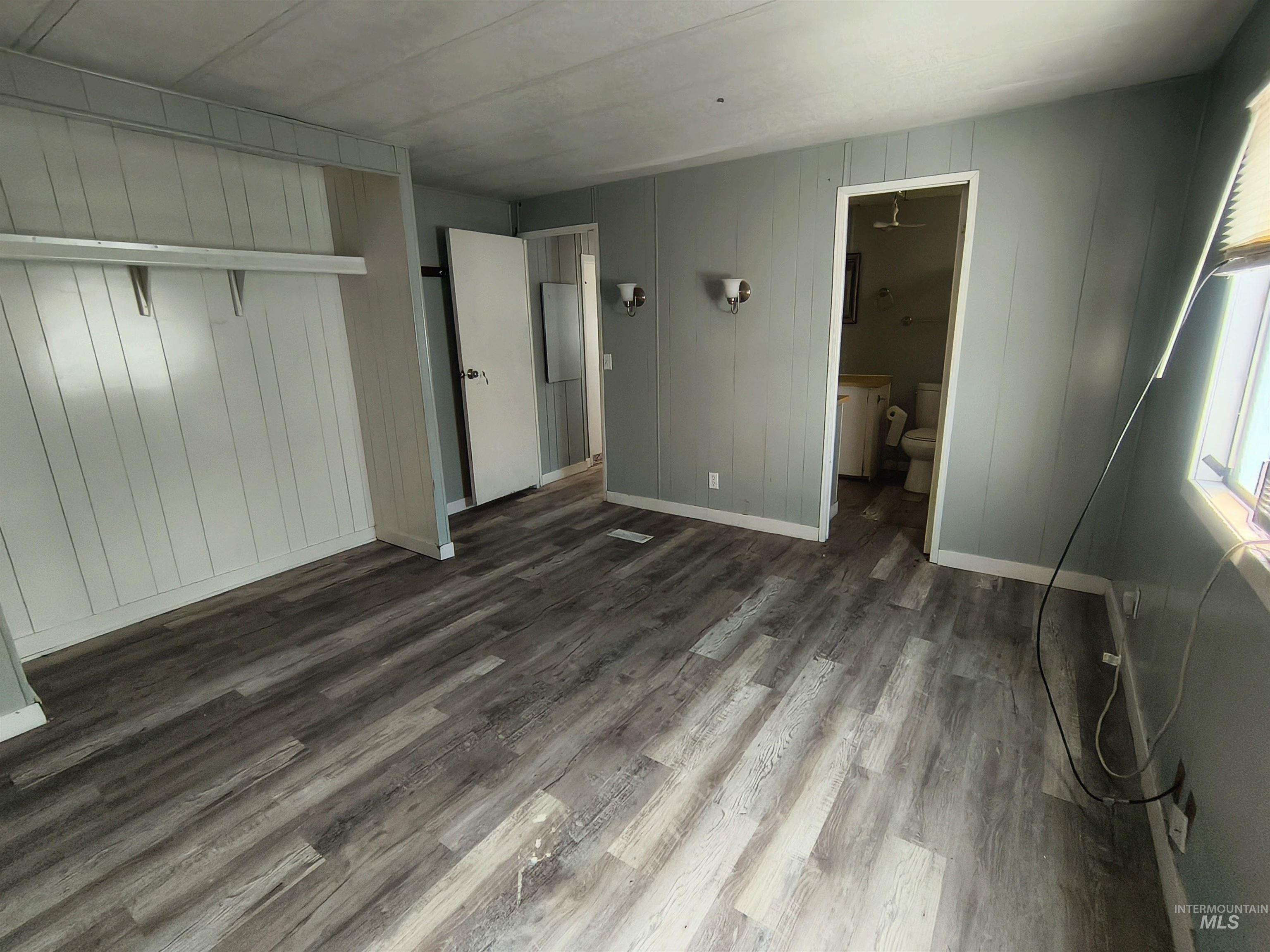 Unfurnished bedroom with wood finished floors, a closet, ensuite bath, and wooden walls
