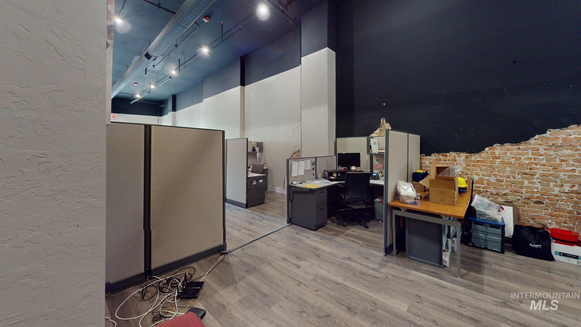 Office featuring light wood-type flooring, a textured wall, and brick wall