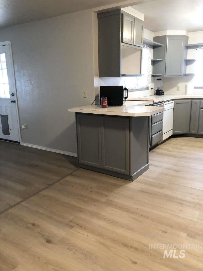 Kitchen with gray cabinetry, light countertops, open shelves, light wood-type flooring, and black microwave