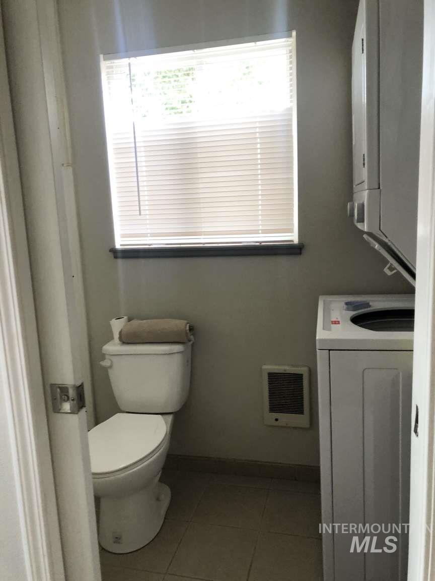 Bathroom with light tile patterned floors, heating unit, vanity, and stacked washing machine and dryer