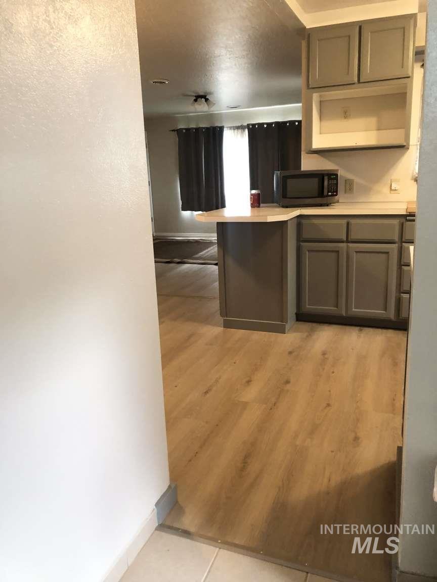 Kitchen with gray cabinets, light countertops, black microwave, light tile patterned flooring, and a peninsula