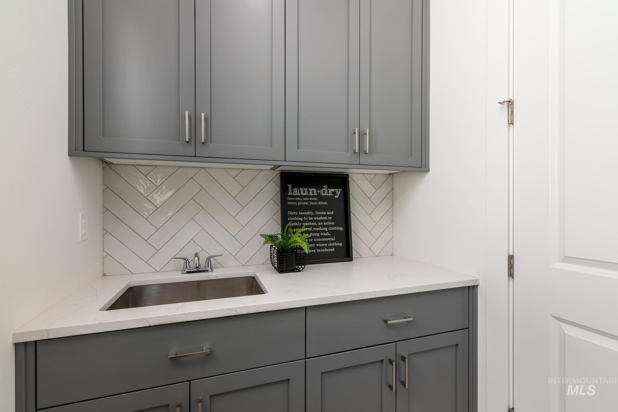 Kitchen with gray cabinets, light stone counters, and tasteful backsplash