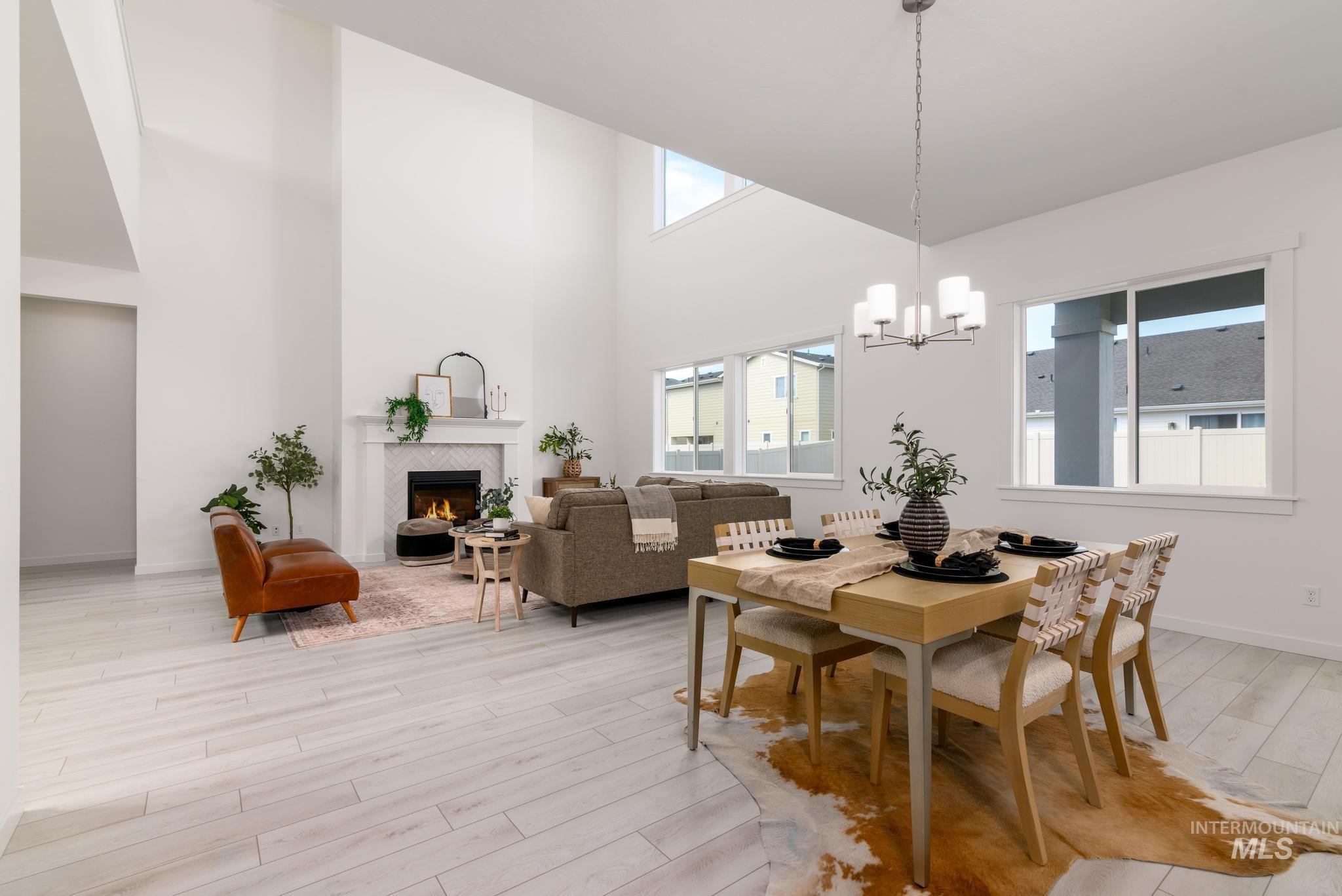 Dining area featuring a tiled fireplace, light wood-type flooring, a towering ceiling, and a chandelier