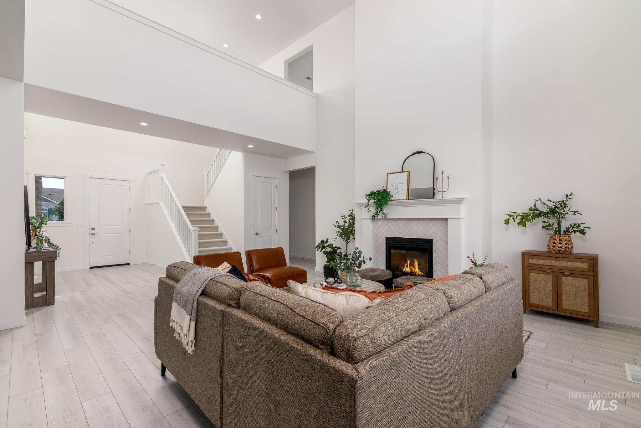 Living area with a high ceiling, light wood finished floors, a tiled fireplace, stairs, and recessed lighting