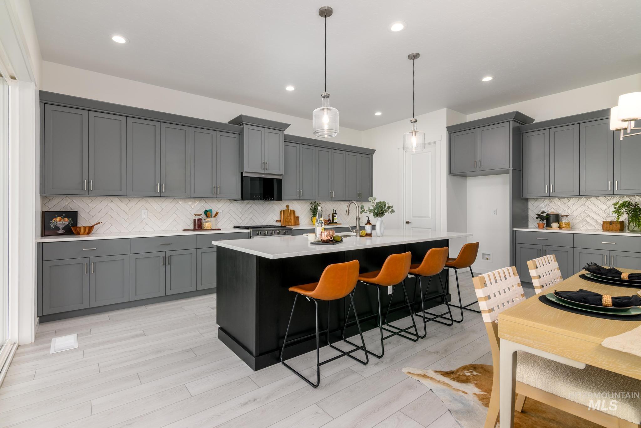 Kitchen with backsplash, a kitchen island with sink, gray cabinets, decorative light fixtures, and recessed lighting