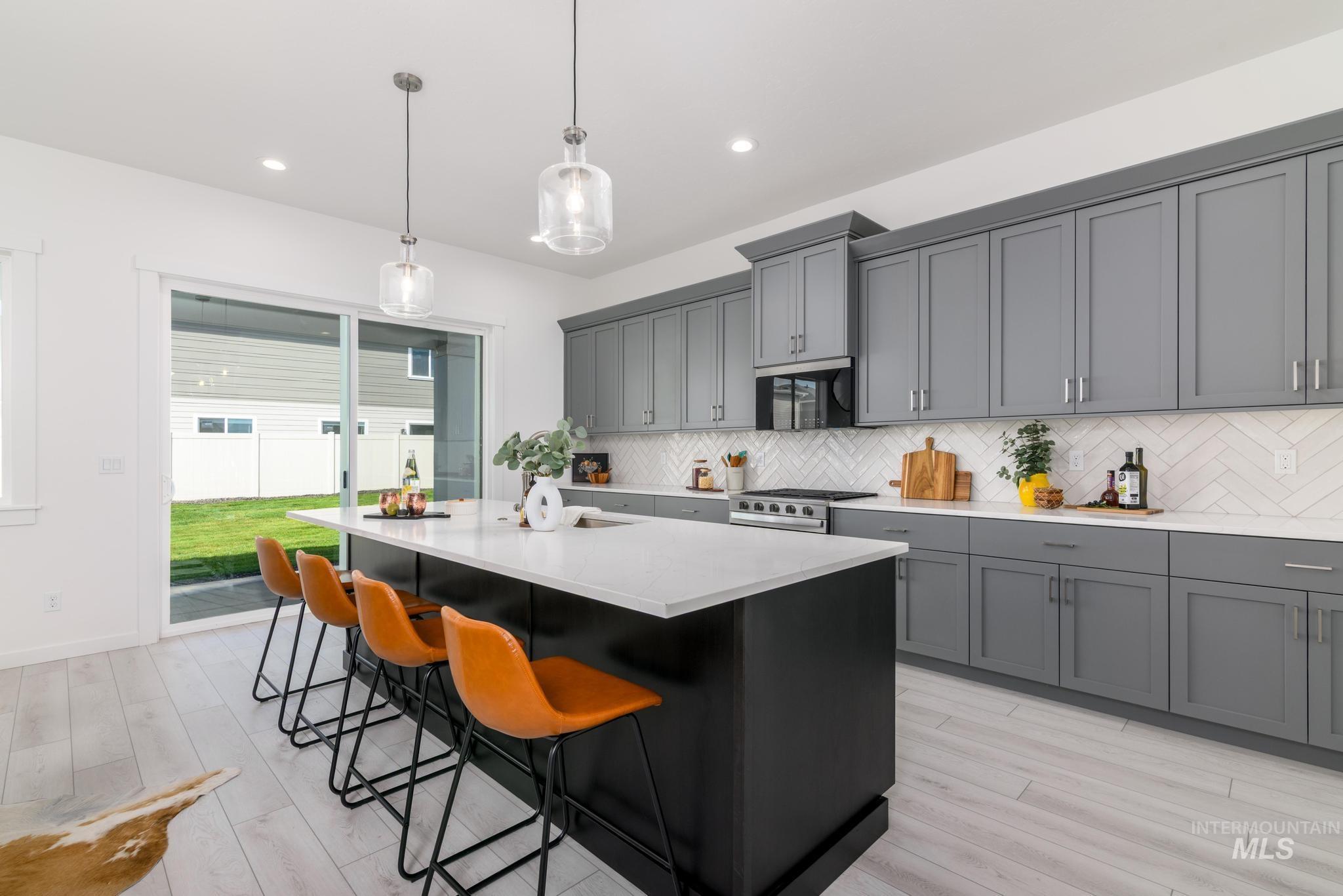 Kitchen with a center island with sink, pendant lighting, gray cabinetry, a kitchen breakfast bar, and backsplash
