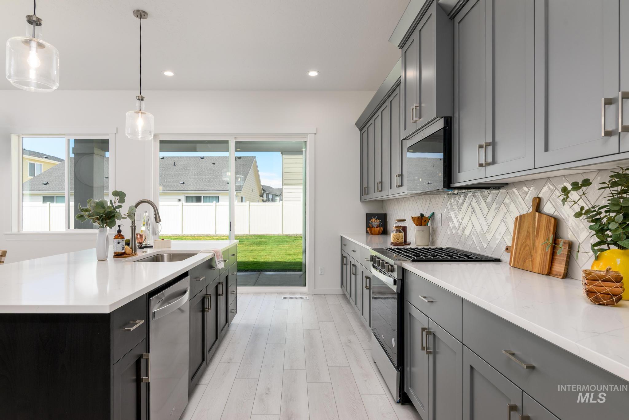 Kitchen with appliances with stainless steel finishes, pendant lighting, light stone counters, recessed lighting, and light wood-style floors