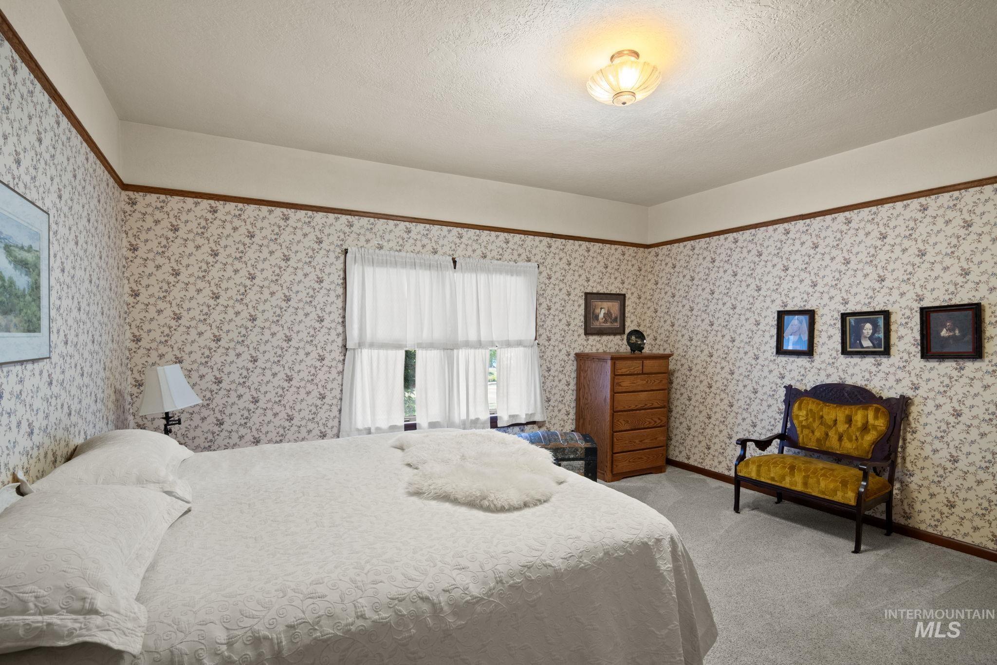Bedroom featuring a textured ceiling, light carpet, and wallpapered walls