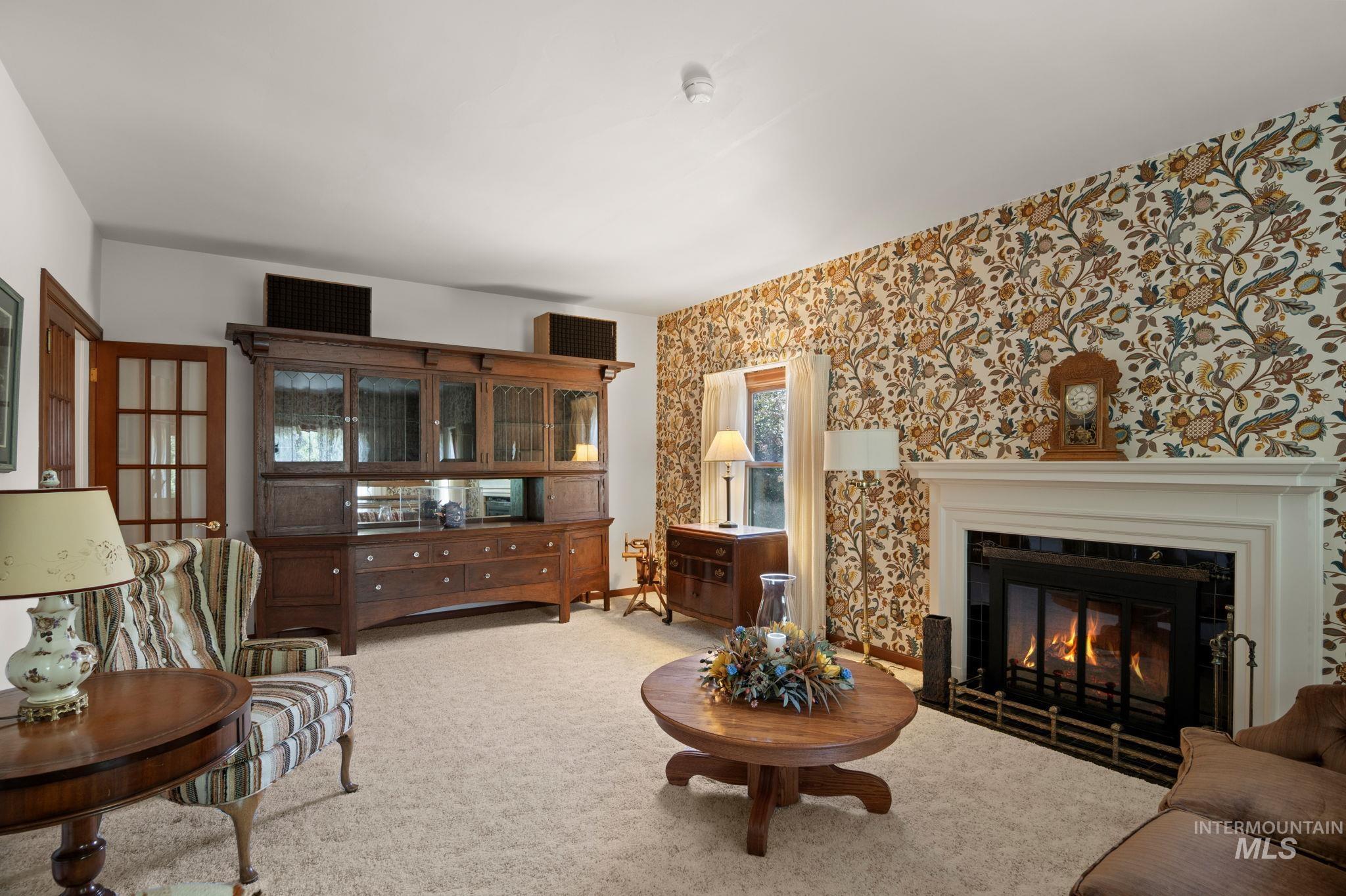 Living area featuring light colored carpet, a glass covered fireplace, and wallpapered walls