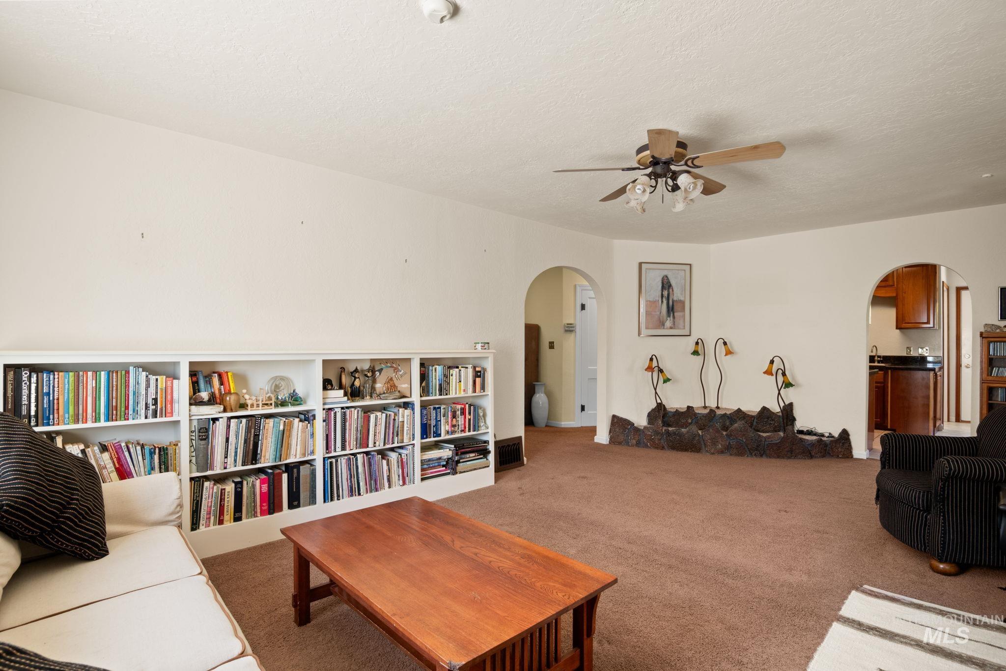 Carpeted living room with arched walkways, a textured ceiling, and ceiling fan