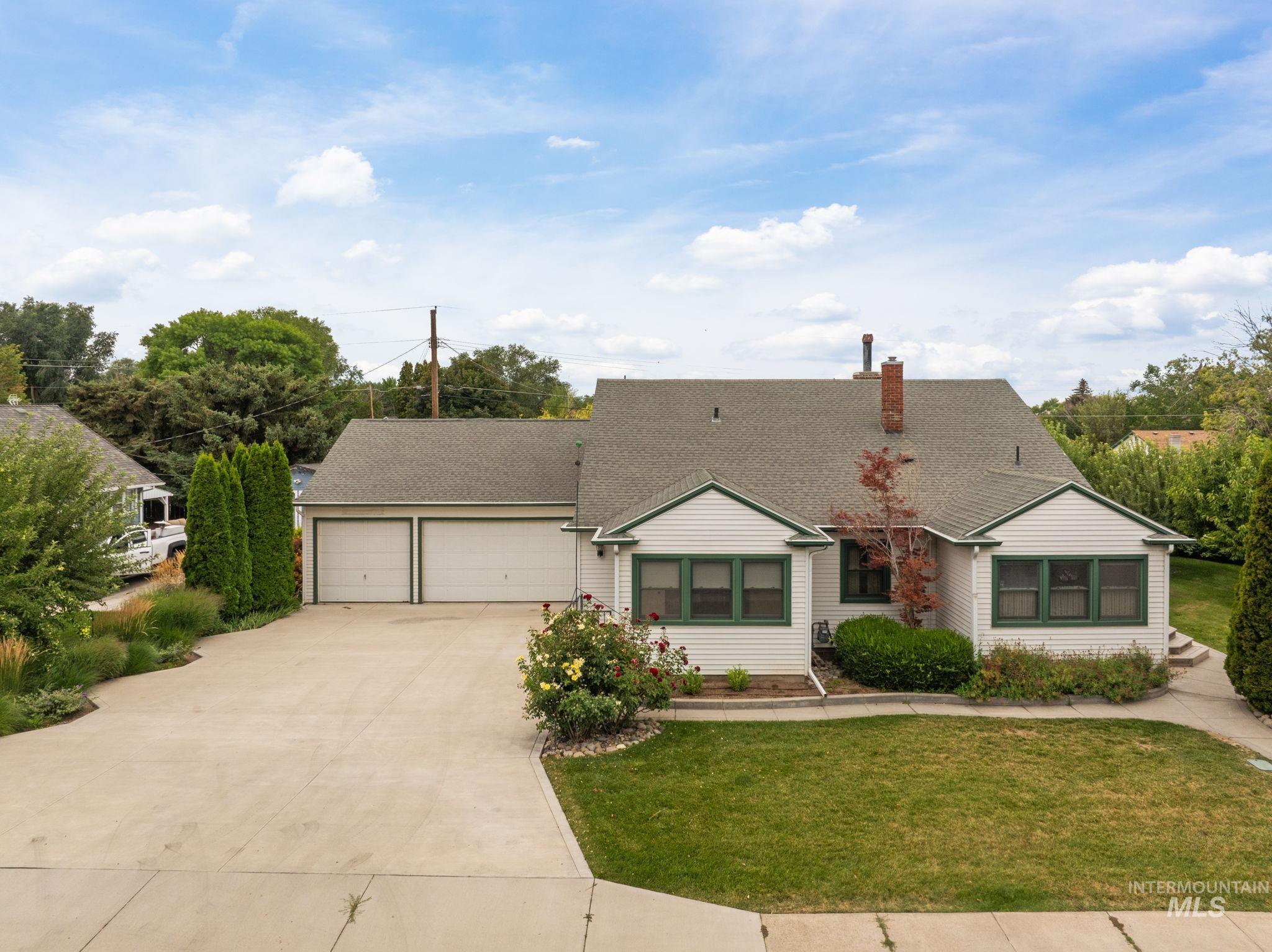 View of front of property featuring driveway, a shingled roof, an attached garage, a chimney, and a front yard