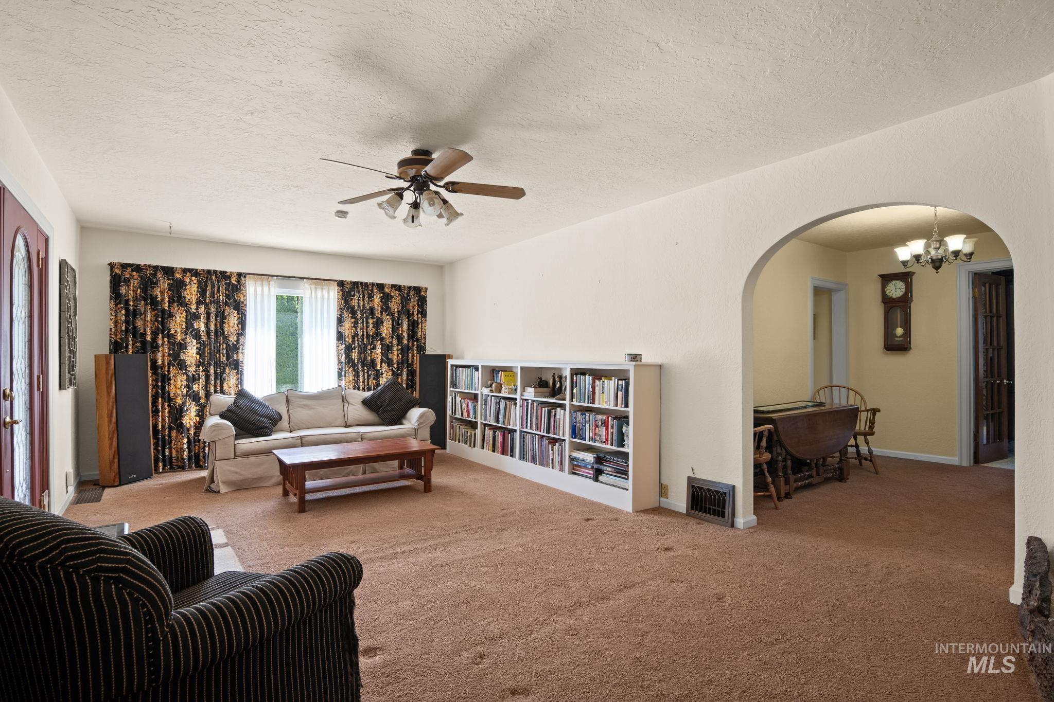Carpeted living room with a textured ceiling, a ceiling fan, arched walkways, and a chandelier