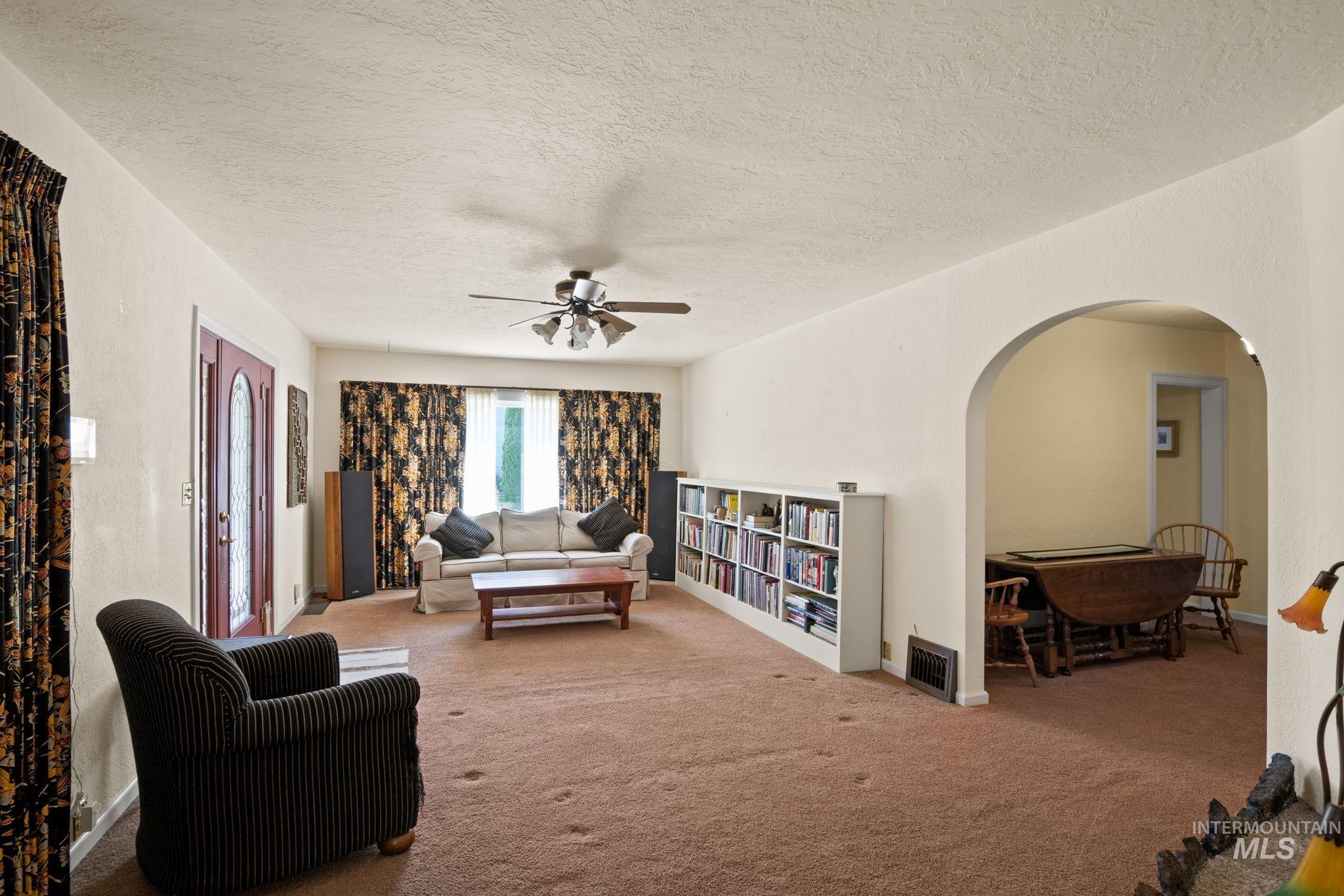 Living area featuring arched walkways, carpet flooring, a textured ceiling, and ceiling fan
