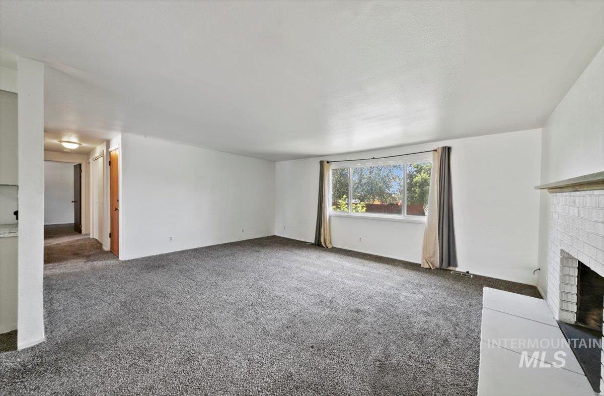 Unfurnished living room featuring carpet and a brick fireplace
