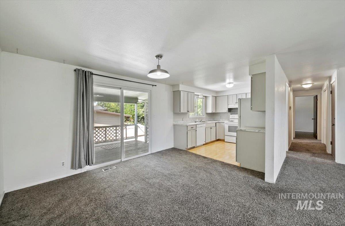 Kitchen featuring light carpet, light countertops, white appliances, open floor plan, and pendant lighting
