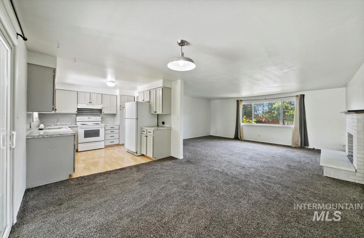 Kitchen with open floor plan, light countertops, white appliances, light carpet, and hanging light fixtures