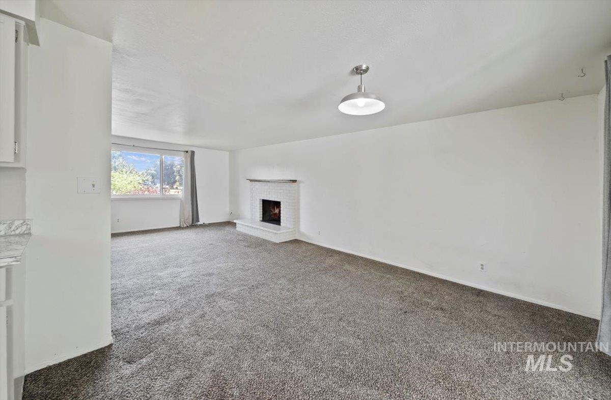 Unfurnished living room featuring a brick fireplace and carpet