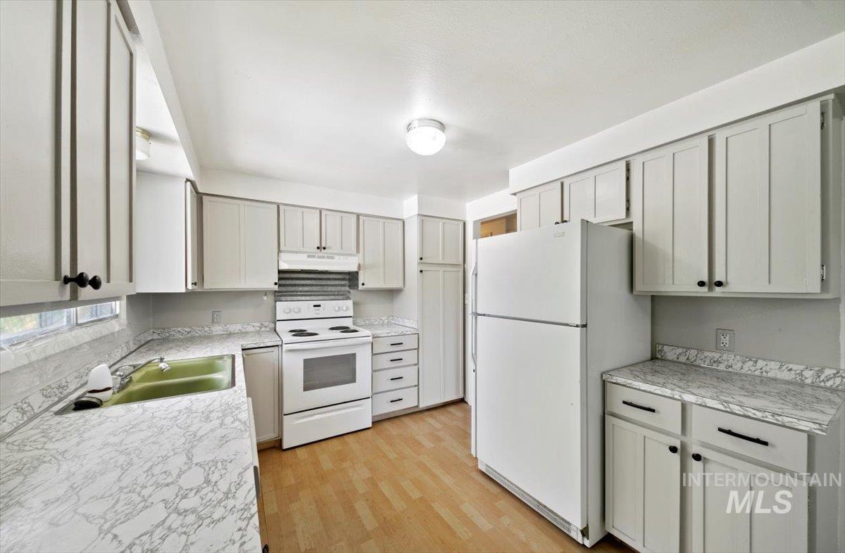 Kitchen with white appliances, light wood finished floors, and under cabinet range hood