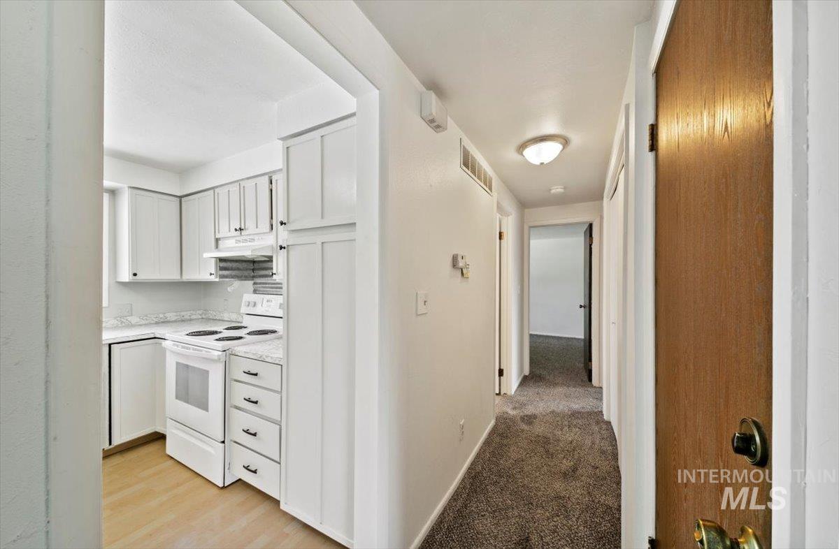 Kitchen featuring white range oven, light countertops, white cabinets, under cabinet range hood, and light carpet