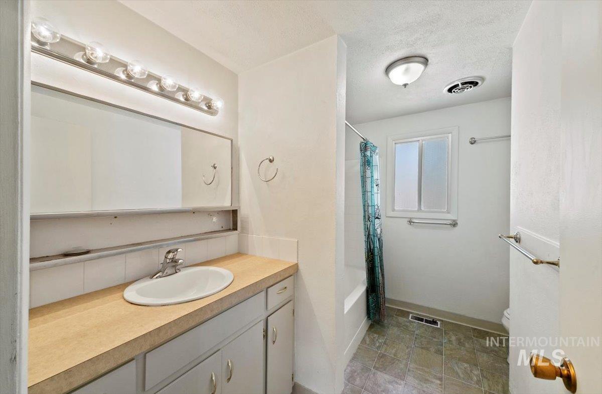 Full bathroom with vanity, shower / bath combination with curtain, and a textured ceiling
