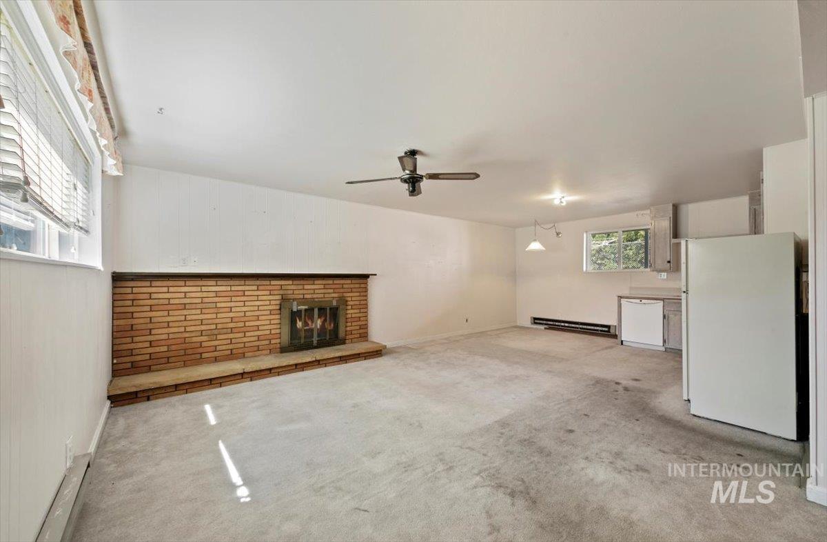Unfurnished living room with light carpet, a fireplace, ceiling fan, and a baseboard heating unit